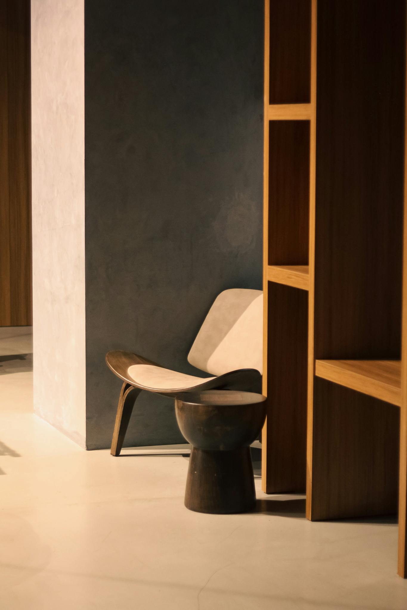 Modern interior featuring a sleek chair and wooden shelves, showcasing minimalist design with warm tones.